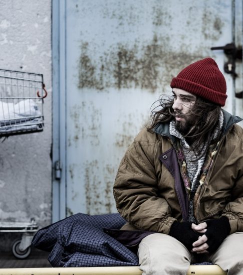 Dirty beggar sitting on night-bag